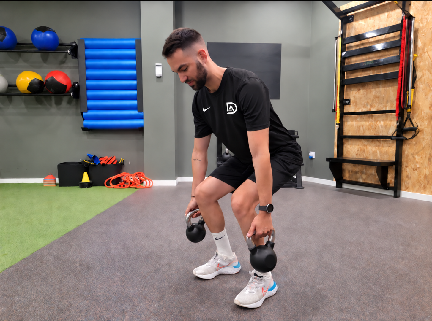 David realizando un ejercicio de fuerza y control con pesas rusas, con camiseta negra personalizada con su logotipo DA
