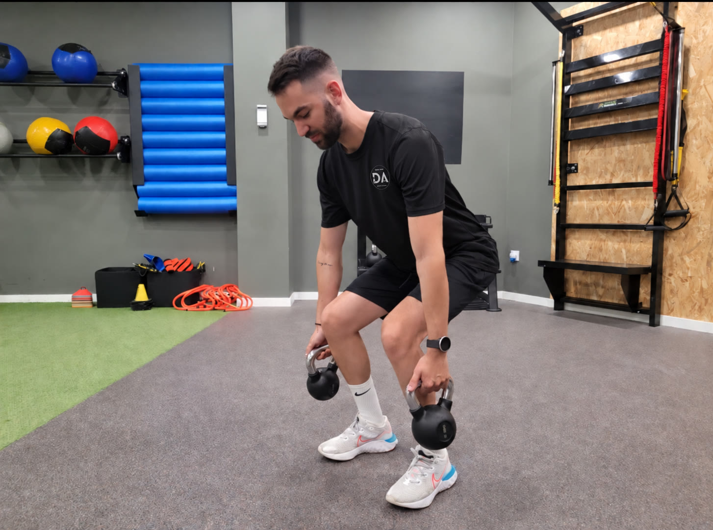 David realizando un ejercicio de fuerza y control con pesas rusas, con camiseta negra personalizada con su logotipo DA
